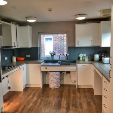 a brightly lit modern kitchen with wood effect floor and a window in the centre