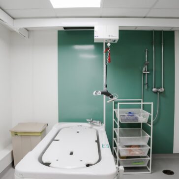 A bathroom with accessible bath and a wet-room shower. There’s trolley next to the bath and a ceiling hoist.