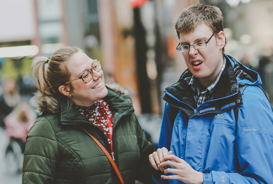 Young man with his support worker standing outside shops in Exeter city centre