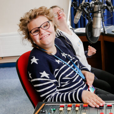 Two college students looking up and smiling whilst sat at a radio station