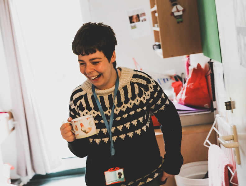 Visually impaired adult smiling whilst in her bedroom enjoying a cup of tea.