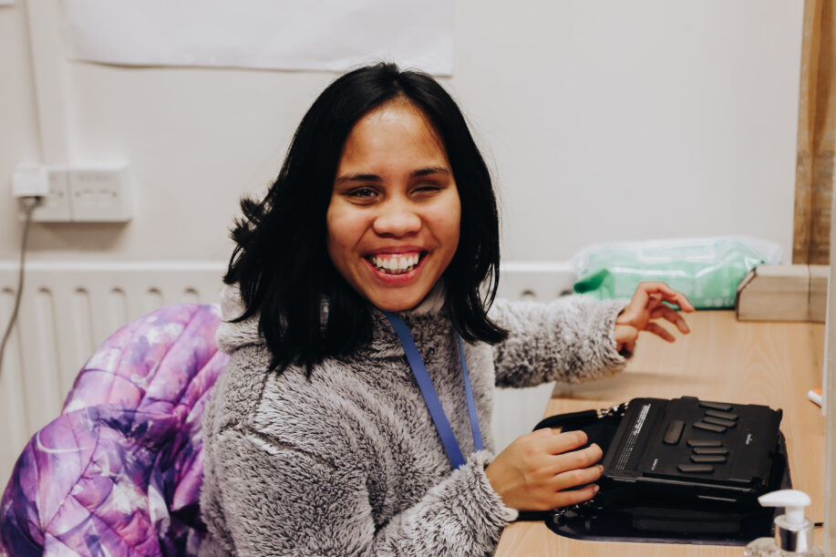 Young lady smiling whilst seated using a braille notetaker