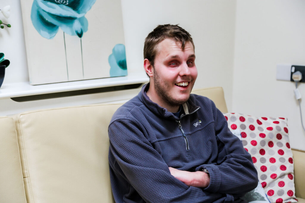 Young man in a sweatshirt sitting on the sofa smiling
