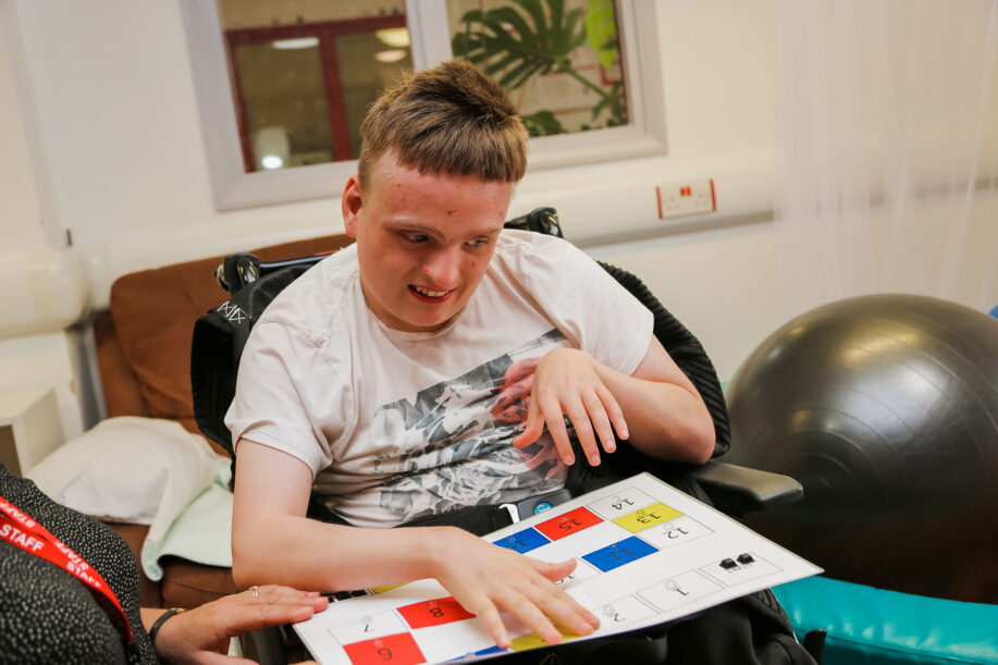 Young man in a wheelchair exploring a tactile piece of paper during a speech and language therapy session
