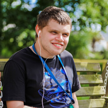 Young man sat on a bench with his headphones in smiling