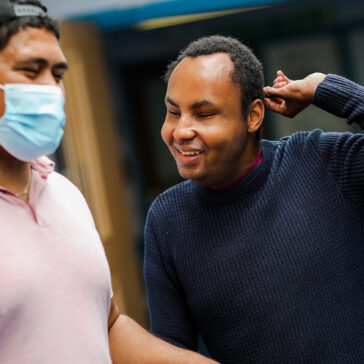 Care worker in a surgical mask and face worker is supporting a smiling young man inside St David’s.