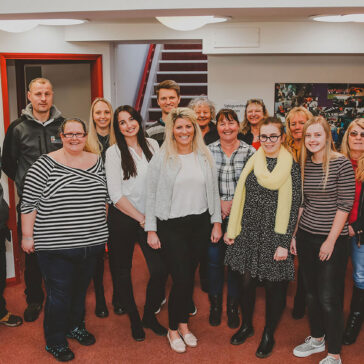 A group of smiling staff standing inside the entrance to St David's House