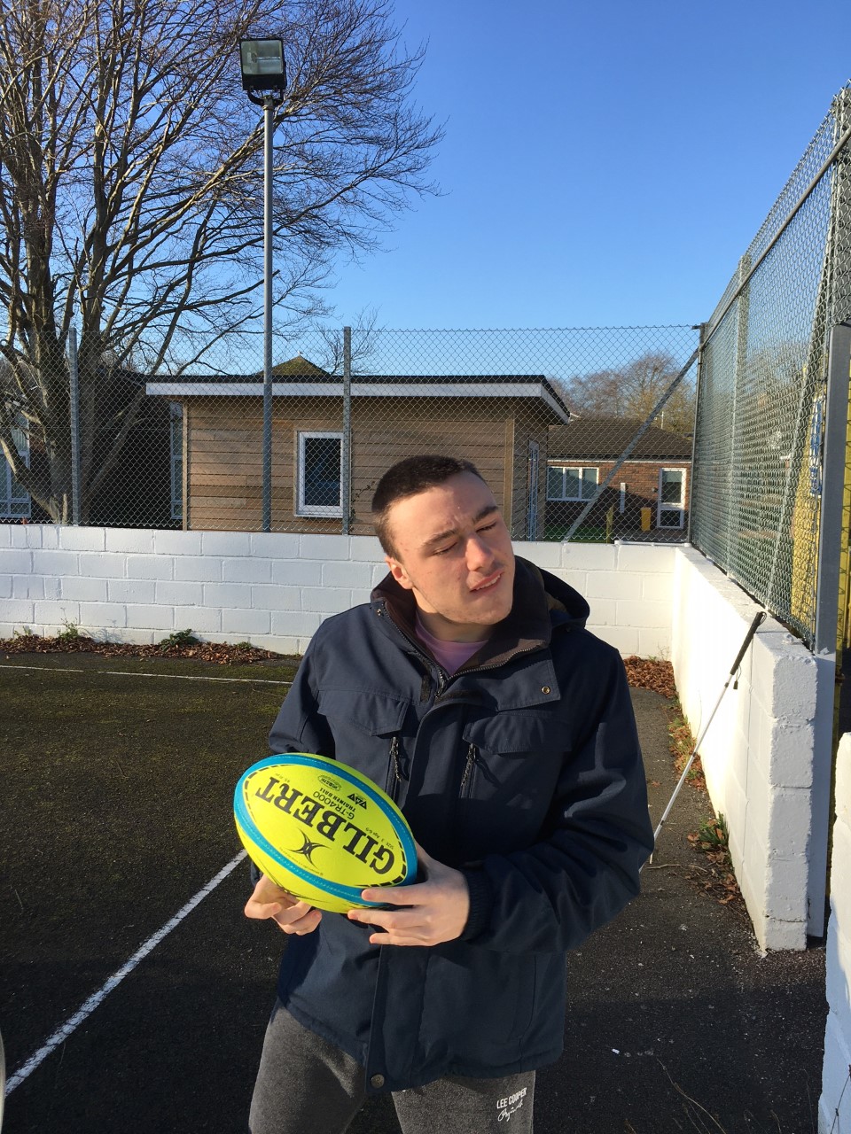 A young man holding a bright yellow rugby ball