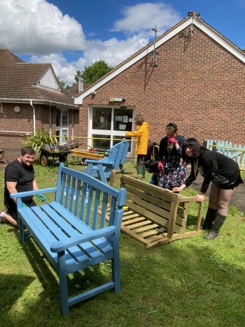 Volunteers outside with three garden benches. Two are already painted pale blue.