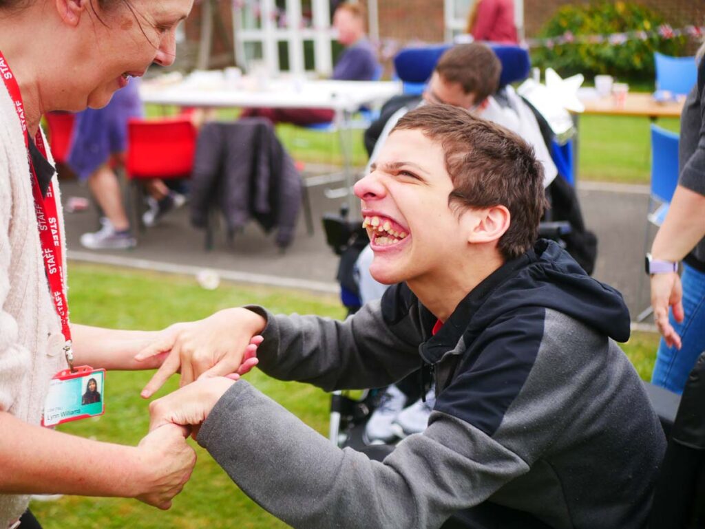 Young man in a wheelchair smiling and looking up whilst holding a support worker's hands