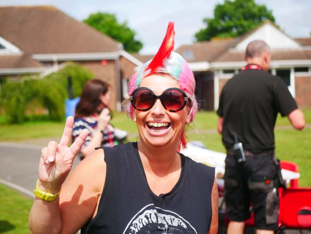 Lady in a mohican wig and sunglasses smiling at the camera outside