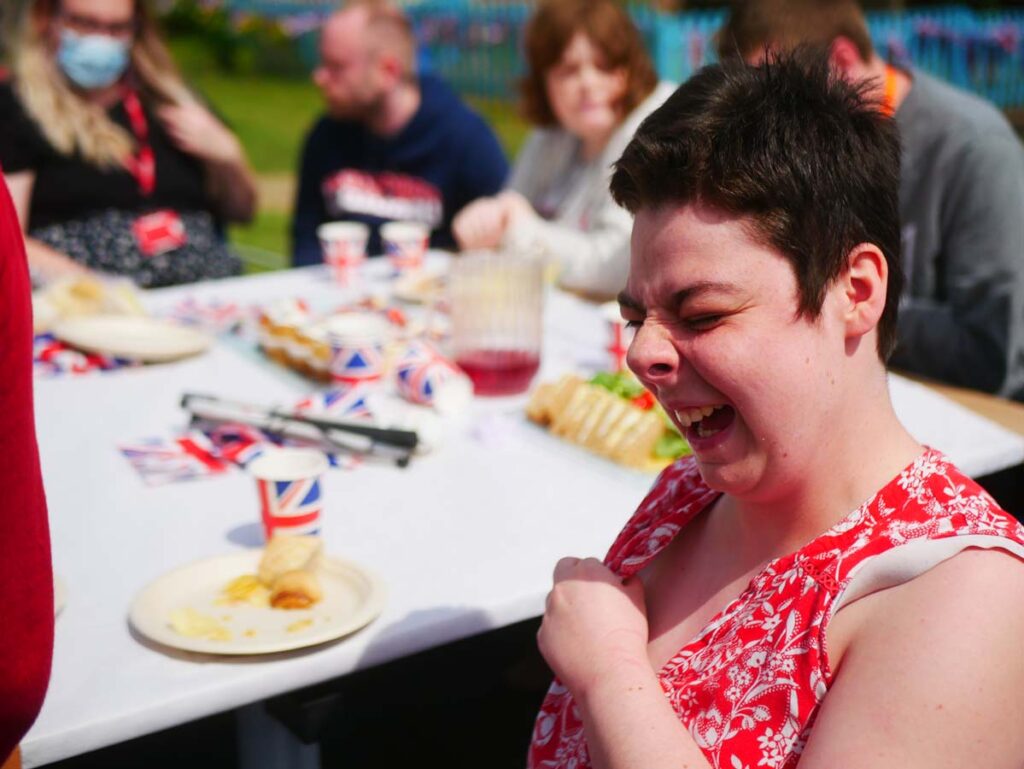 Young lady enjoying a joke. There's a table of street party food in the background.