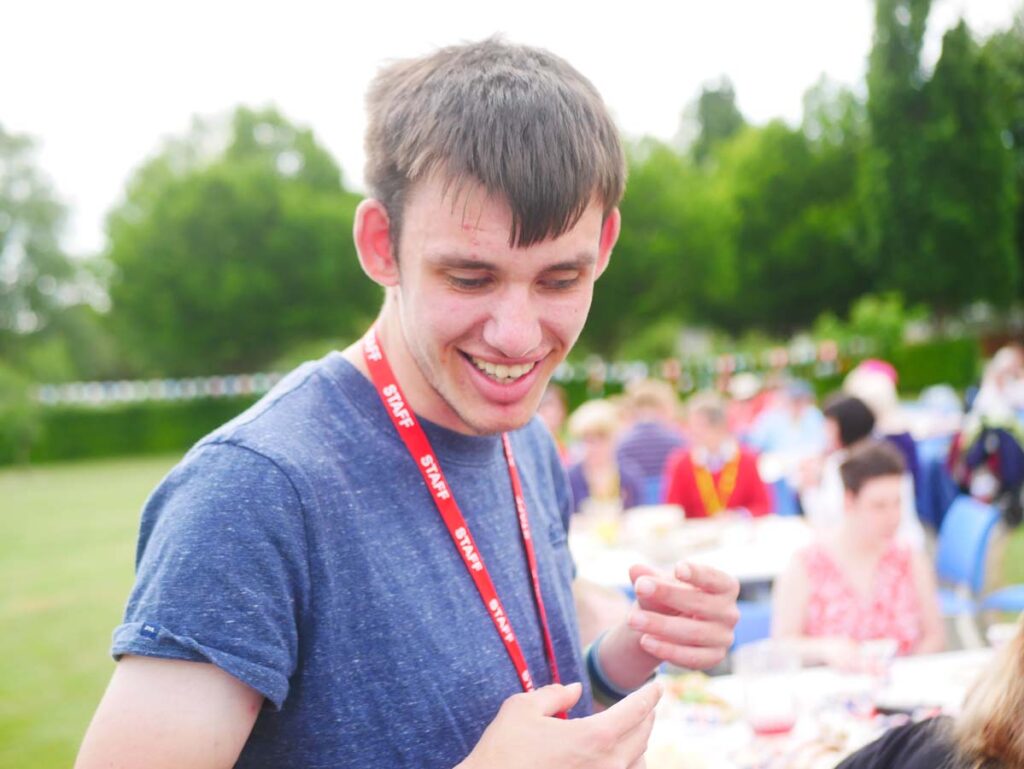 Young man smiling with several tea part tables and guests in the background