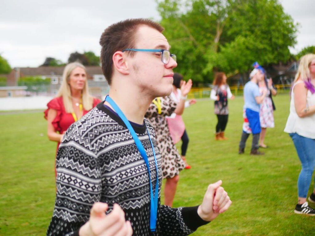 Young man in glasses outside dancing with people behind