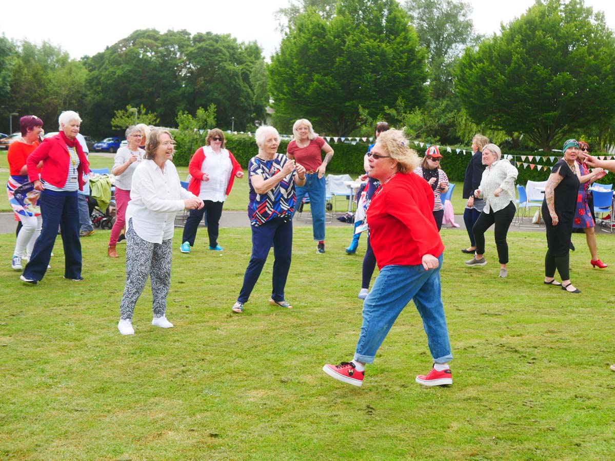 Group of people dancing outside on the lawn with bunting in the background