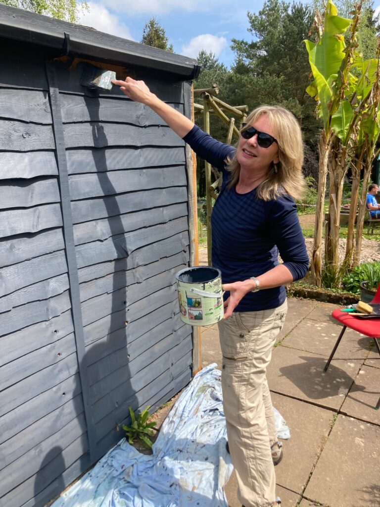 Lady in sunglasses painting the outside of a shed