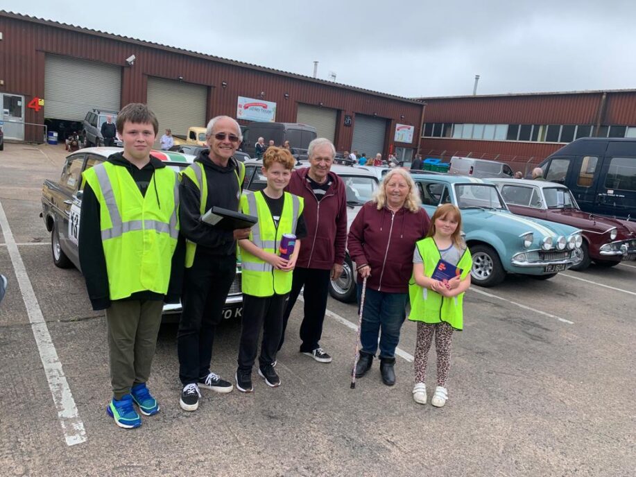 Five people standing outside in front of a line of cars