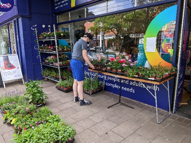 Young person organising a display of plants on a table outside shop
