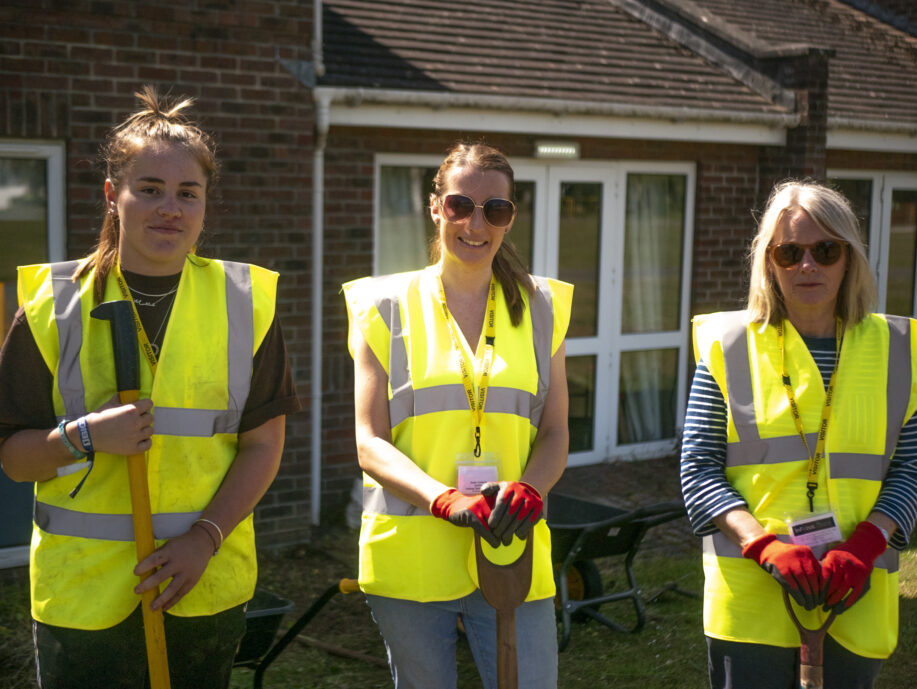 Three ladies wearing high visibility jackets standing outside a house