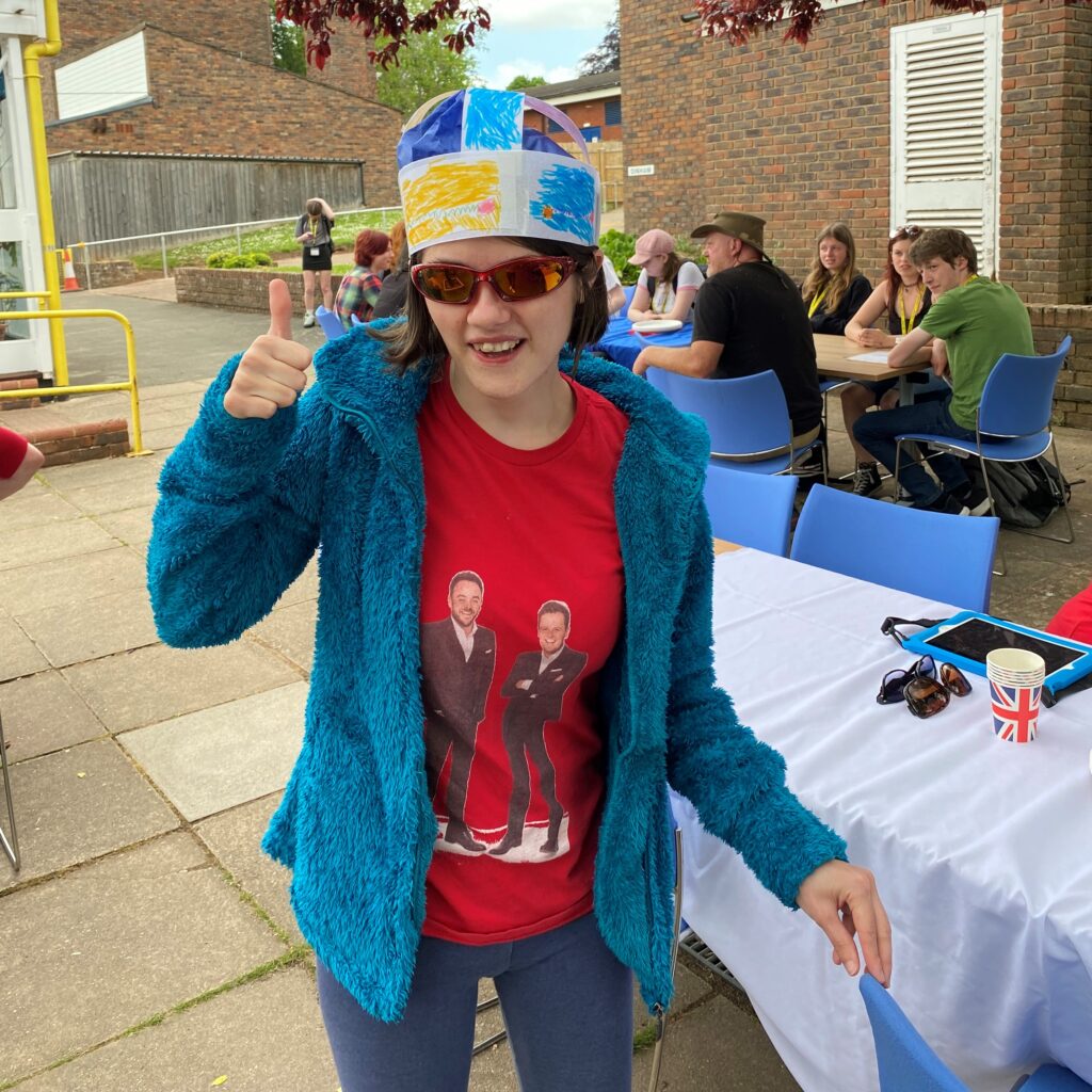 A young woman with her thumb up. She's wearing a paper crown.