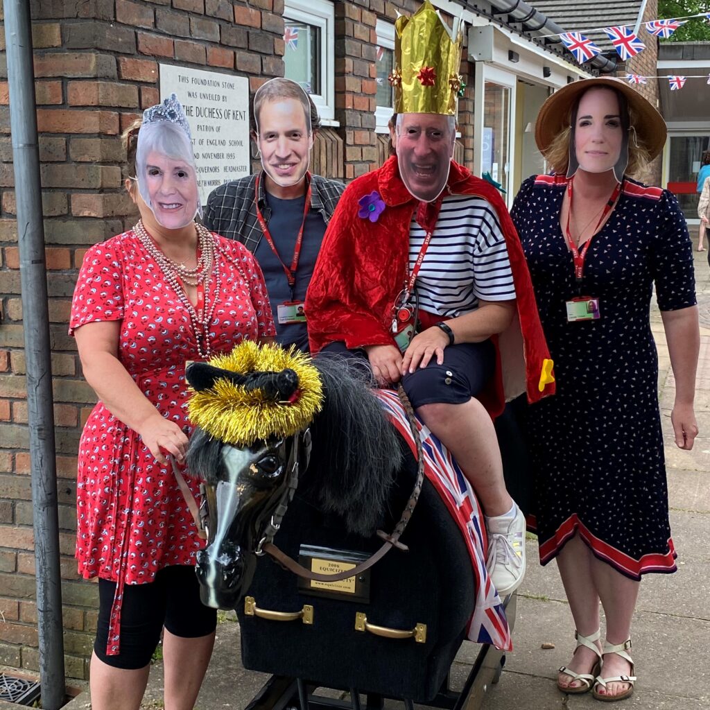 Four people wearing masks of the Royal Familiy and a rocking horse.
