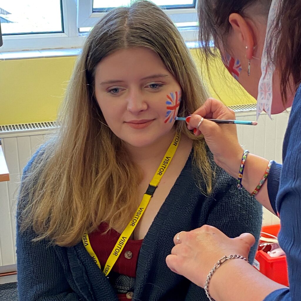 A young woman having her face painted with a union jack