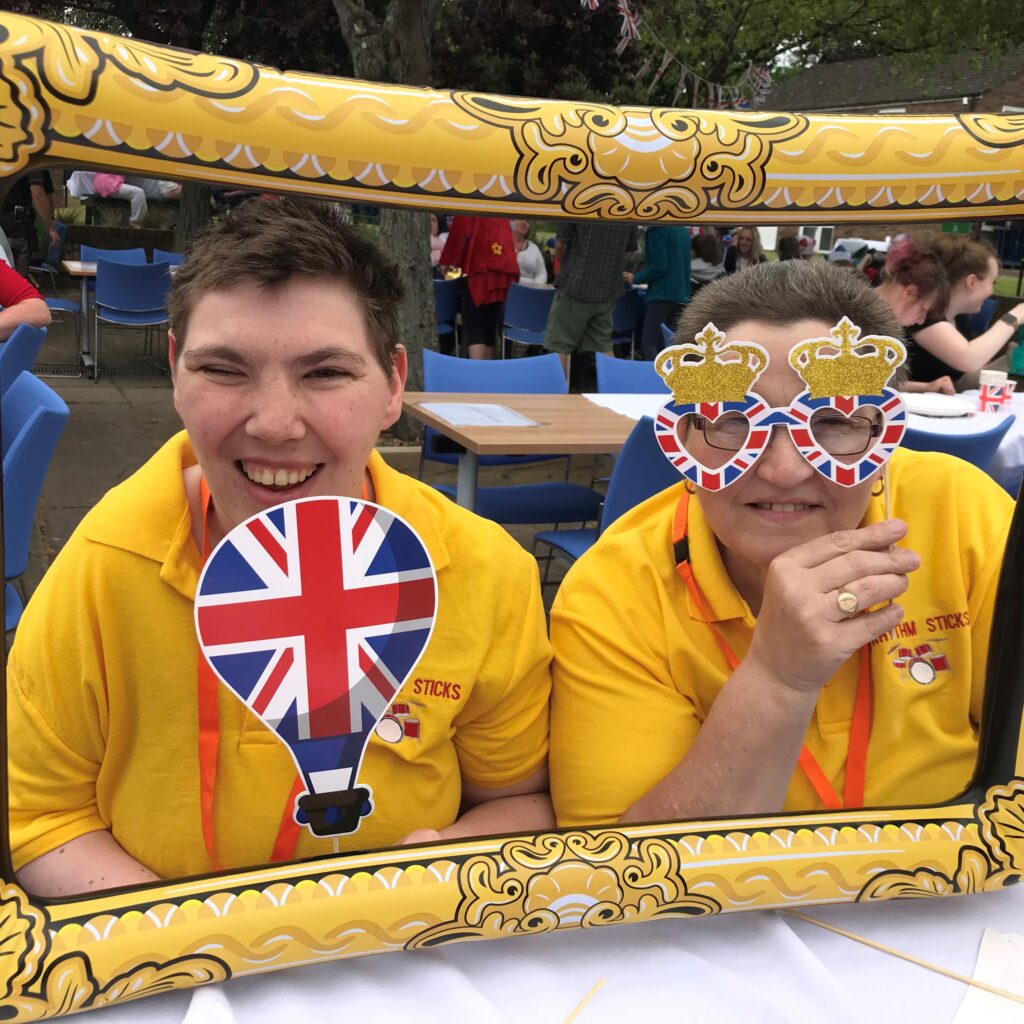 Two people holding up cardboard union jack glasses and a flag. Surrounded by a blow up frame.