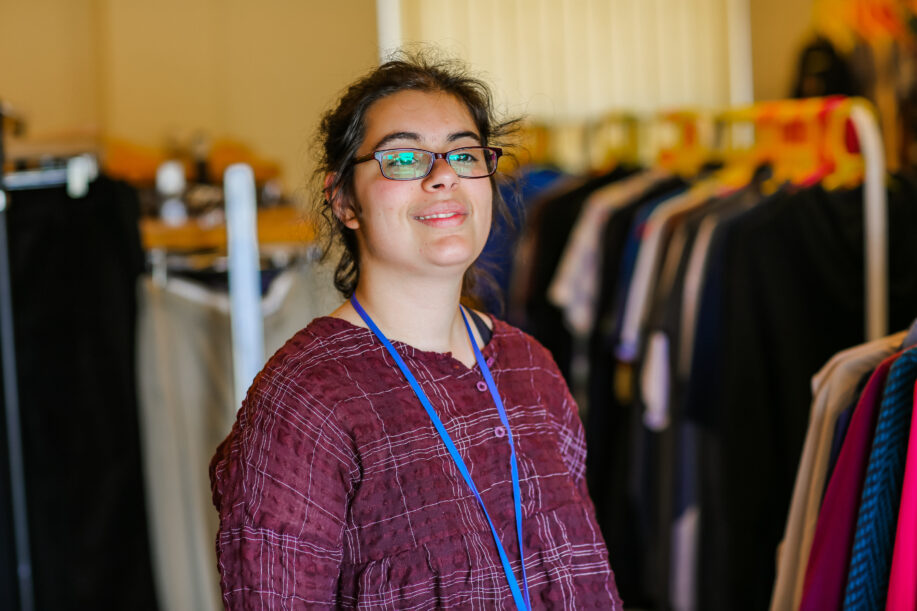 Young person looking away from the camera into the light. In the background there are clothes hanging from rails.