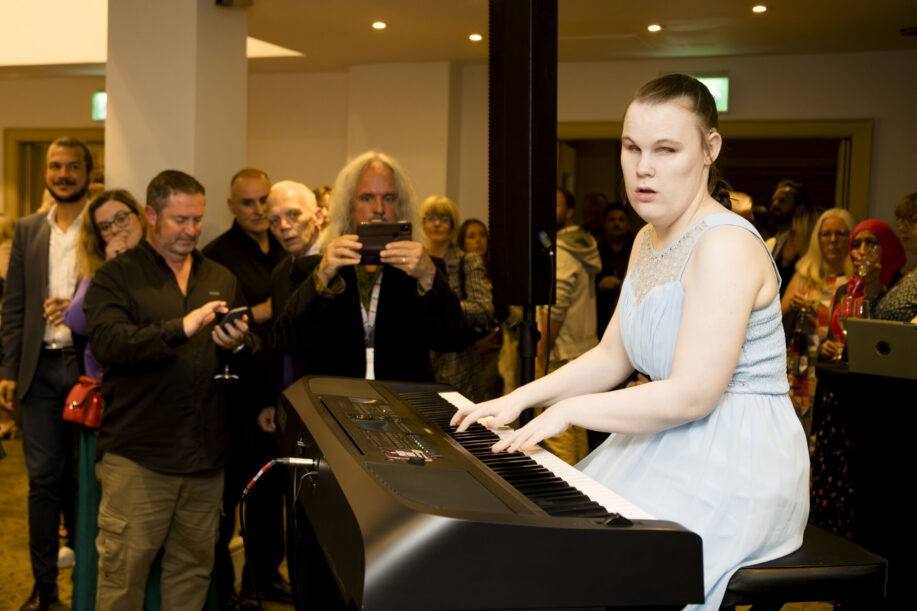 Young woman playing a piano in front of a crowd.