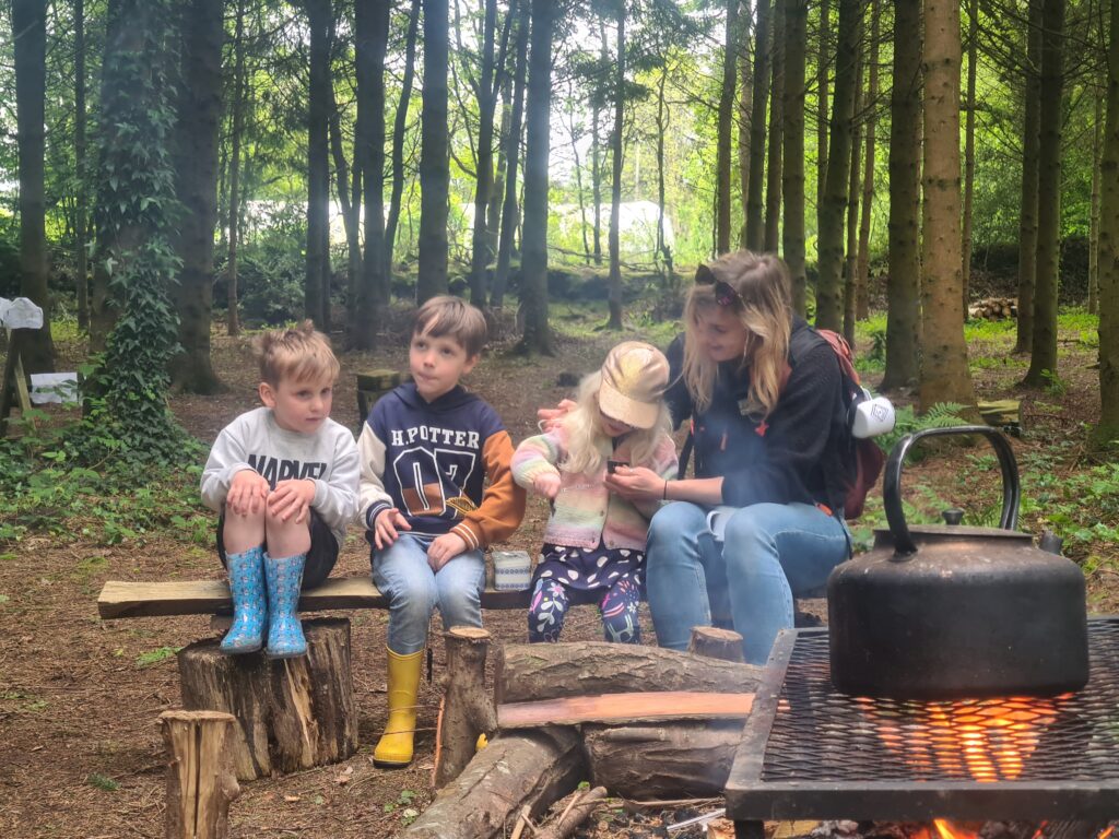 Three children and a lady sit on a bench in woodland