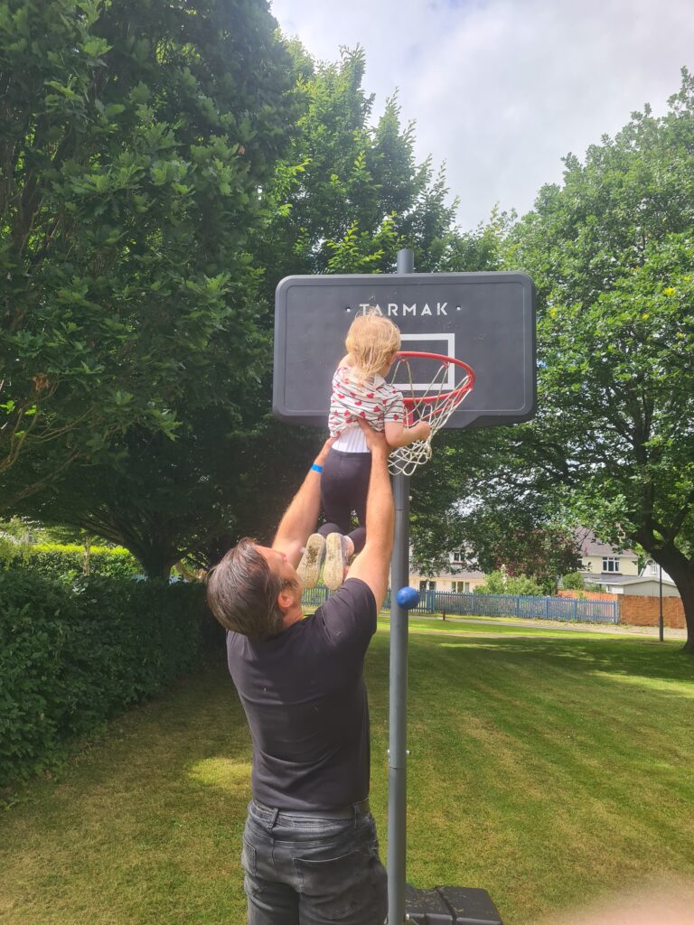 A man holds up a toddler to a basket ball net.
