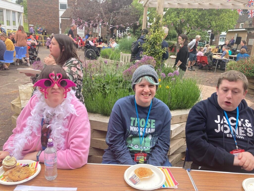 Three young people sat outside. One is wearing glamourous pink sun glasses.