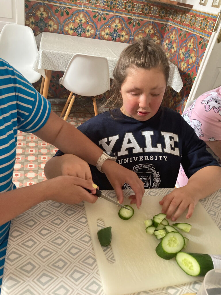A young woman is chopping a cucumber with assistance.