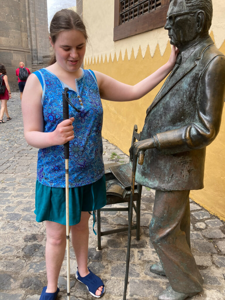 A young woman with a cane touches a statue of a man
