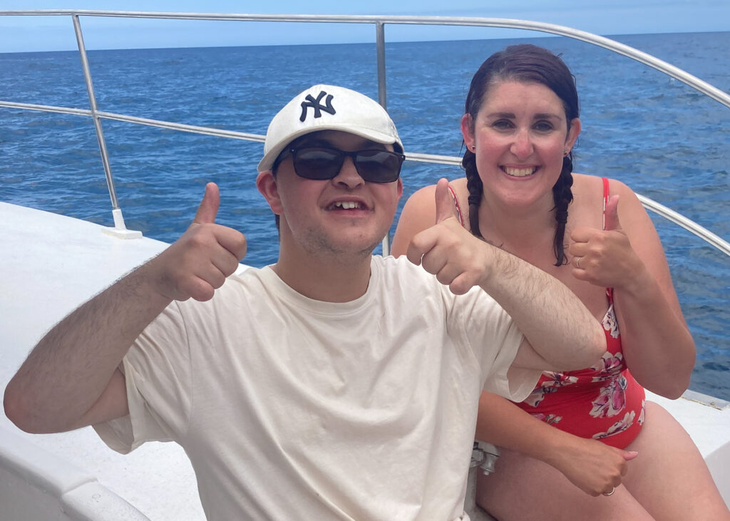 A young man and a lady on a boat at sea. They both have their thumbs up.