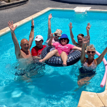 A group photo of young people and adults in a pool. They all have their arms in the air.