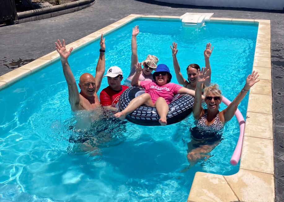 A group photo of young people and adults in a pool. They all have their arms in the air.