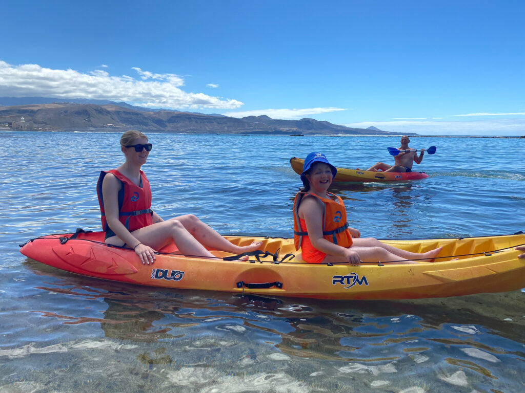 Two young women in a kayak at sea. There's another kayak behind with a man.