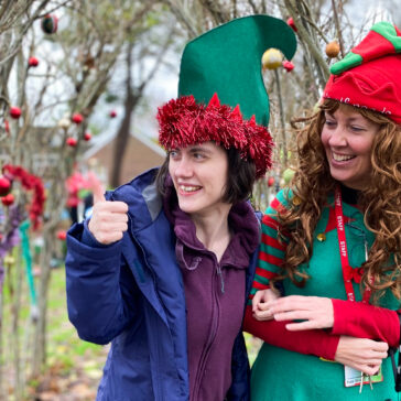 A young adult and an adult stood outside - both dressed as elves.