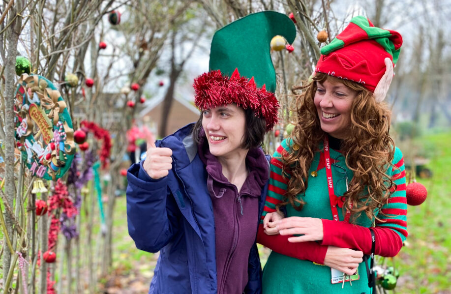 A young adult and an adult stood outside - both dressed as elves.