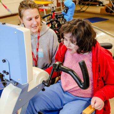 A young woman sat on a exercise bike and a support worker