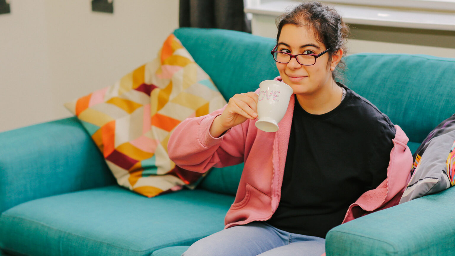 A young woman sat on a sofa drinking from a mug