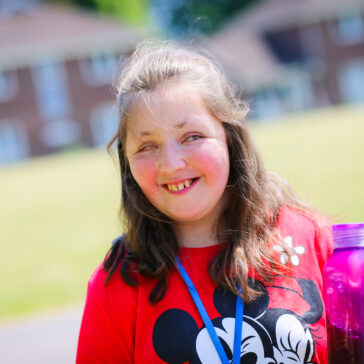 Young woman holding a drinks bottle, standing outside in the sunshine.