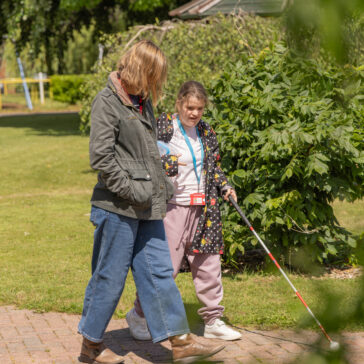 A student using a cane is walking along with a support worker