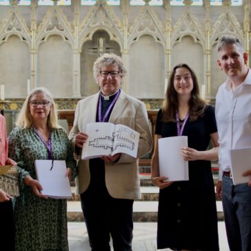 Five people standing in a catherdral. They are all facing the camera and holding braille guides