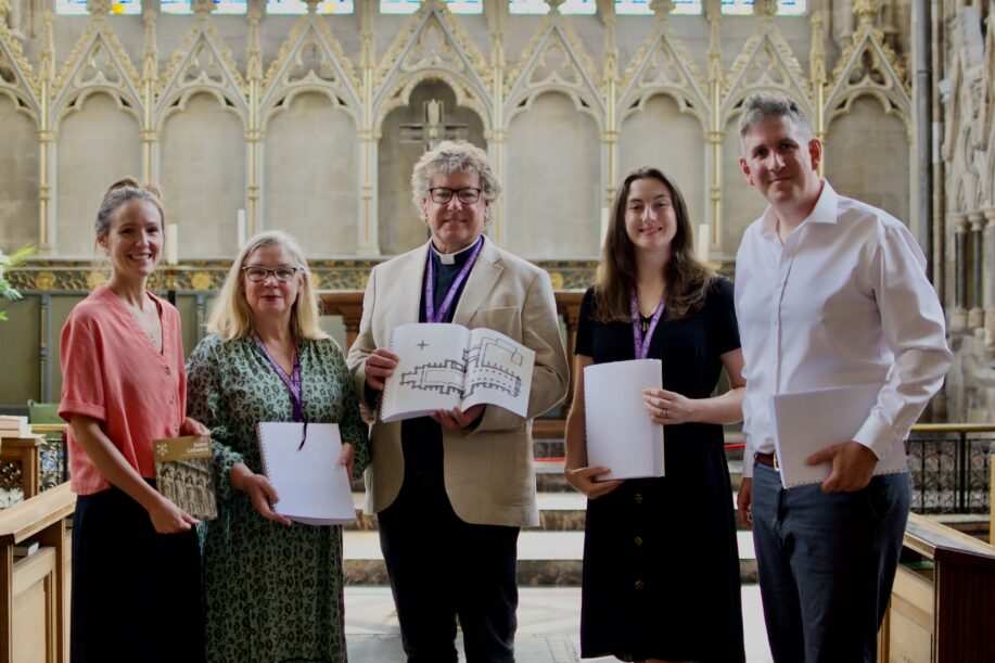 Five people standing in a catherdral. They are all facing the camera and holding braille guides